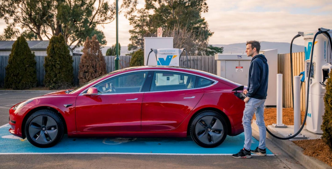 An image of a man charging his electric vehicle at an Evie charging station.